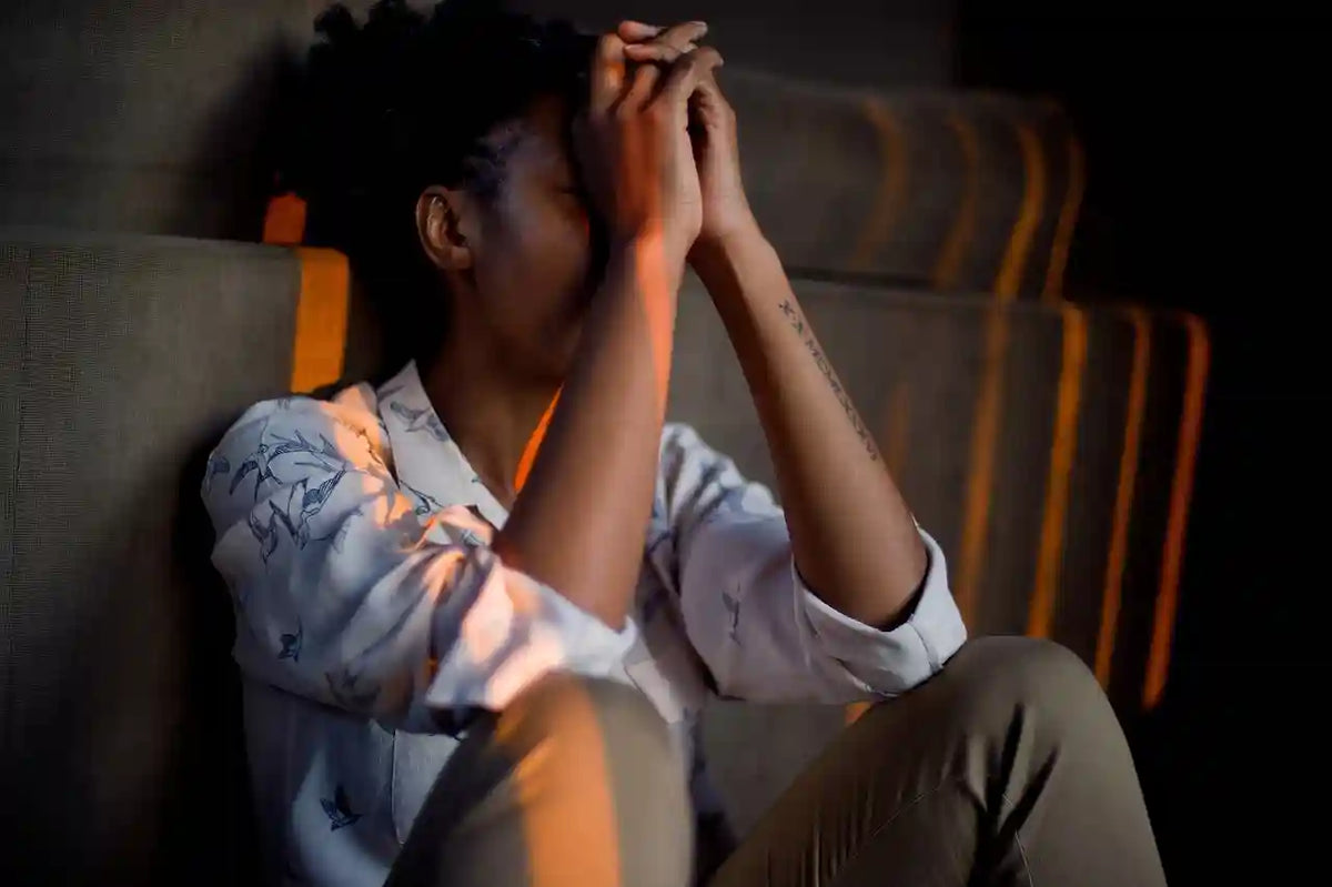 Stressed African American woman sitting alone, head in hands, reflecting the impact of hormonal imbalance on mental health