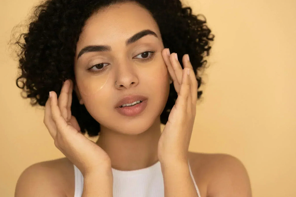 Woman touching face while checking for collagen deficiency symptoms, shown against a warm beige background