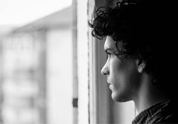 Man looking out window in deep thought, representing brain fog and anxiety awareness