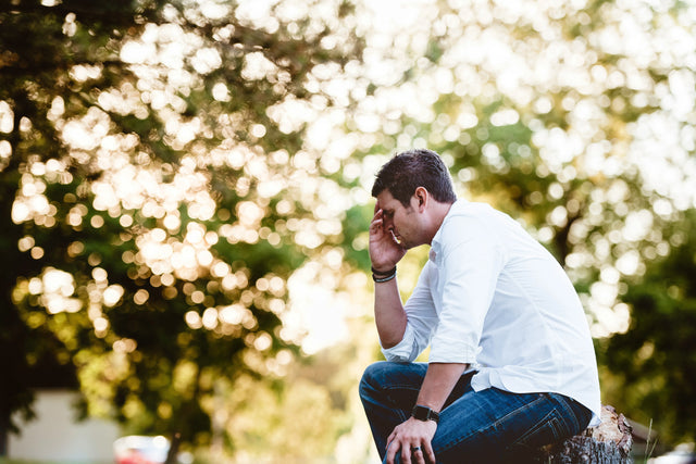 Man sitting outdoors holding his head, reflecting frustration because of histamine overload symptoms.