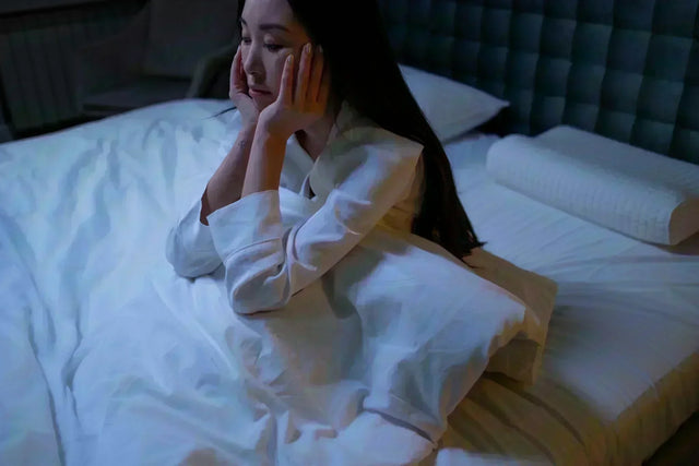 Woman in white sleepwear seeking ways to prevent insomnia while sitting on bed at night